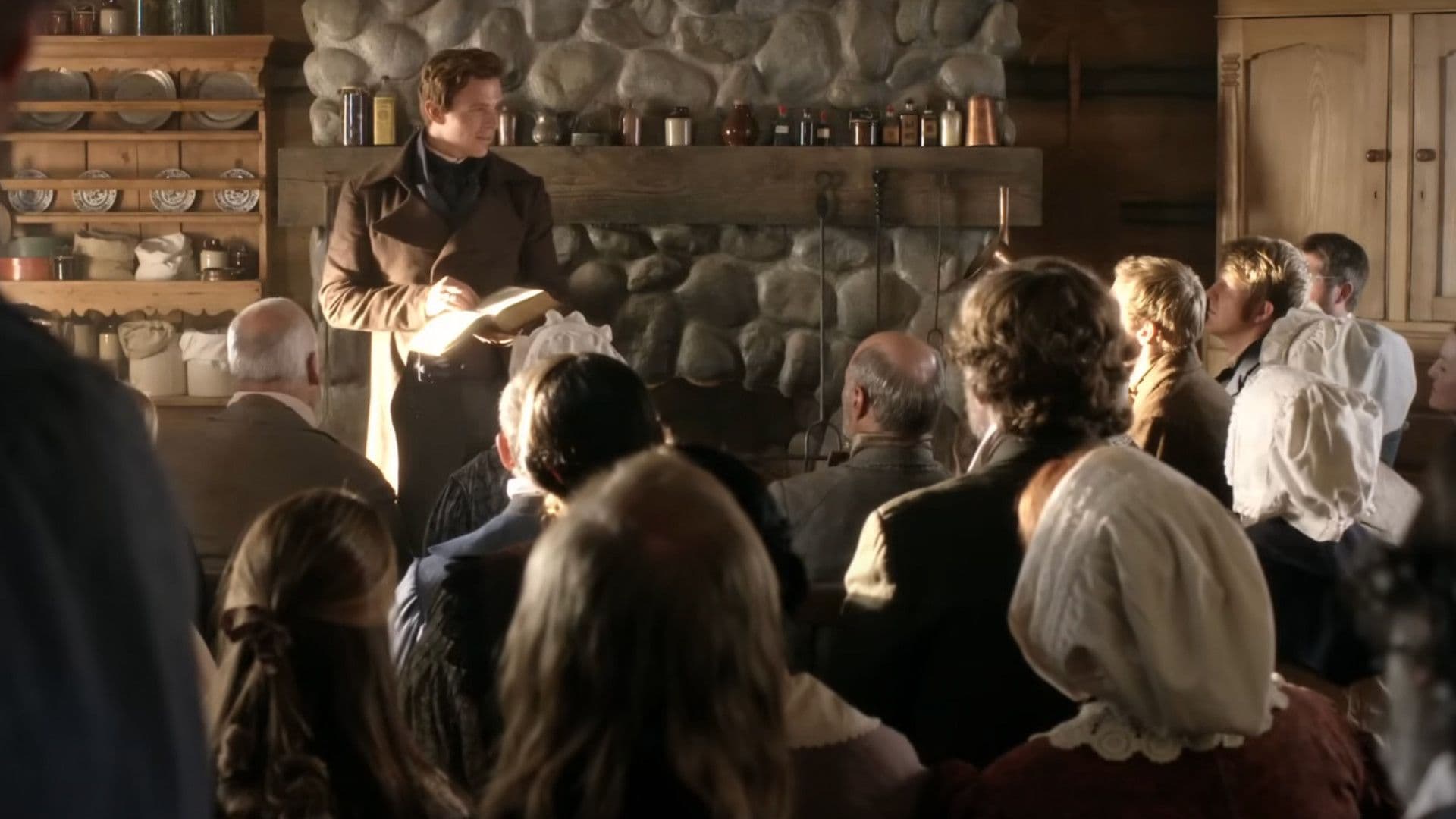 José Smith de pie frente a un grupo de personas en una pequeña cabaña de madera en un fotograma de "Un día para las eternidades", una película publicada por la Iglesia de Jesucristo de los Santos de los Últimos Días.