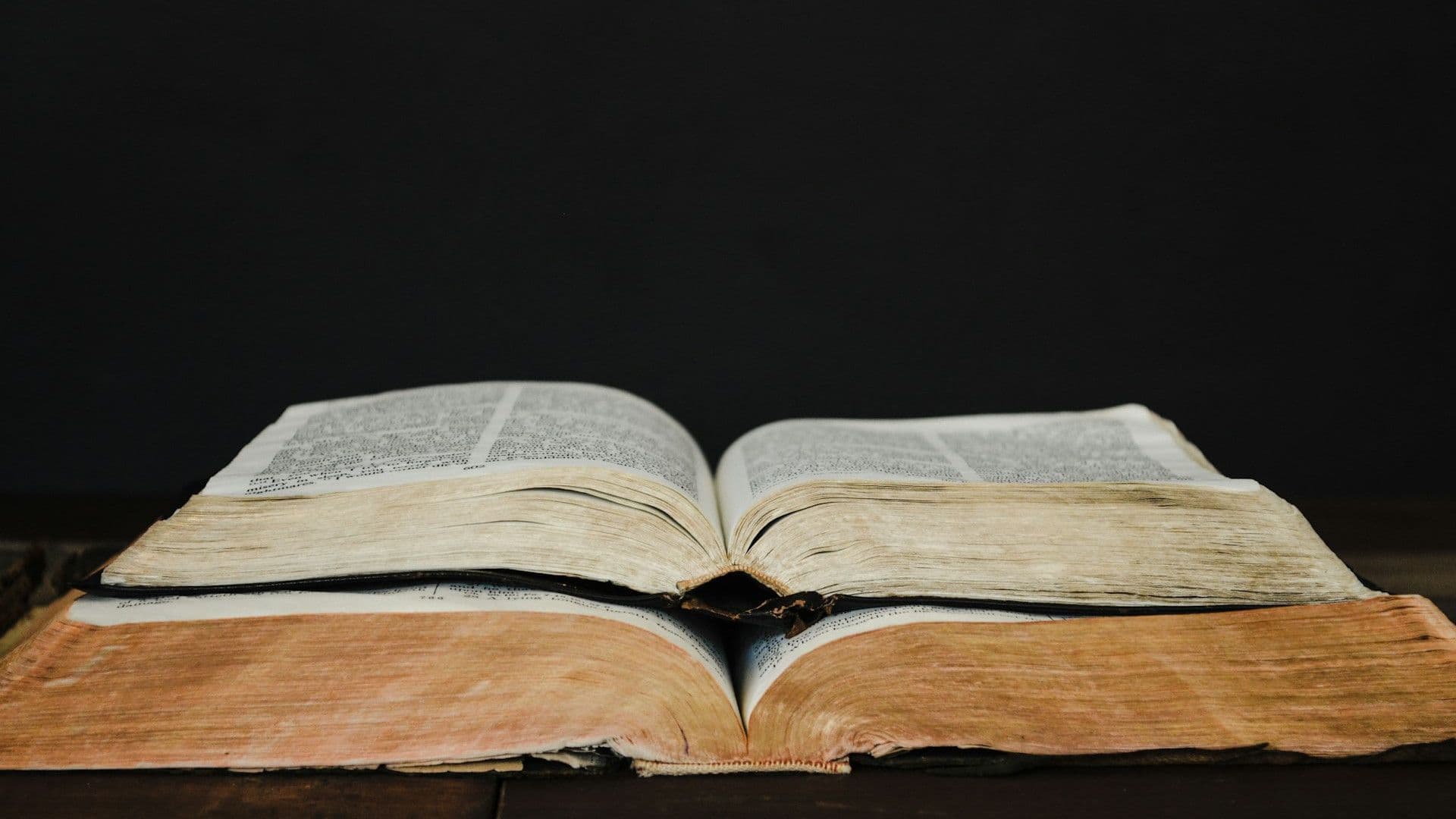 Dos libros abiertos, uno encima del otro, sobre fondo negro